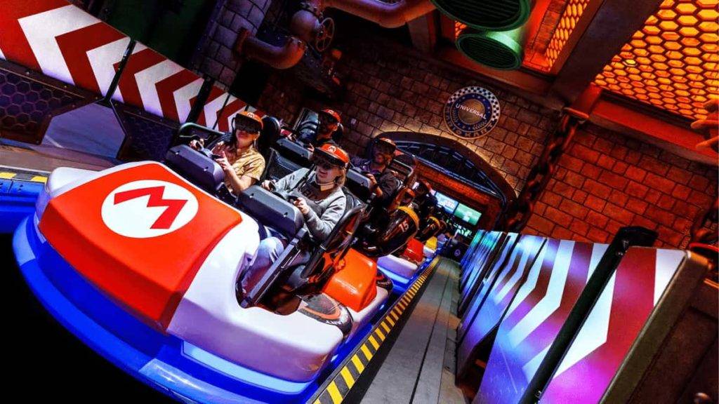 Riders with VR glasses sit in Mario Kart themed indoor roller coaster cars, wearing AR glasses.