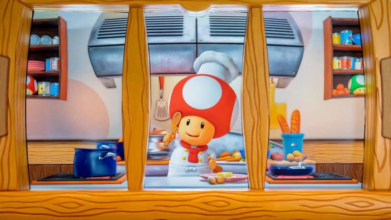 A holographic Toad in a chefs uniform poses with ingredients behind a wooden divider.